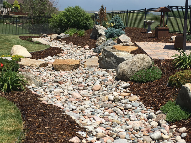 Partial xeriscape design with a pave stone patio, mulch ground covering, and custom rock swale and walkway in Leydon Ranch, Colorado. 
