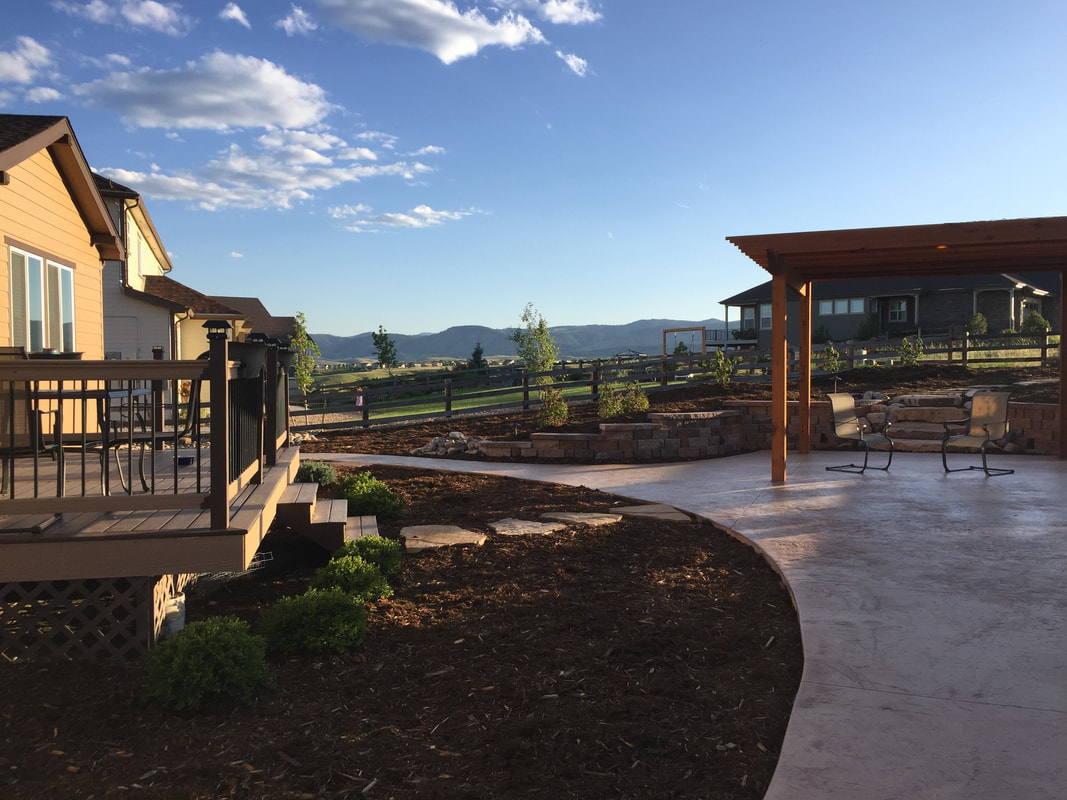 A custom stamped concrete patio and walkway with flagstone path and wooden pergola for a home in Leydon Ranch, Colorado with xeriscape design. 