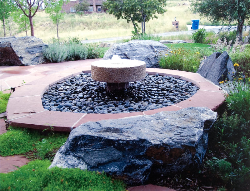Endless outdoor fountain with river rock and brick perimeter for backyard in the Denver metro. 