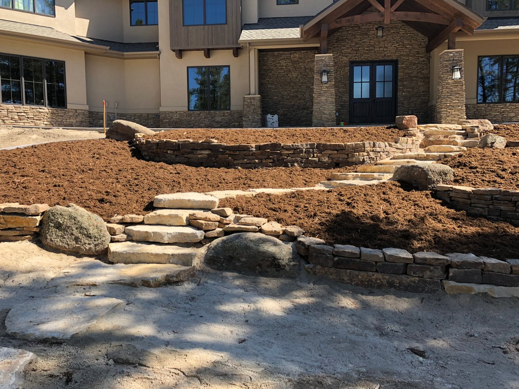 Photo of a terraced front yard using river rock retaining walls and custom outdoor stepped staircase for a stately mountain mansion using ground covering for a drought resistant landscape in Arvada, Colorado. 