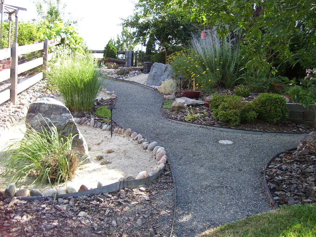 Colorful garden xeriscape with shrubs, boulders, blossoming perennials, and a gravel walkway.  