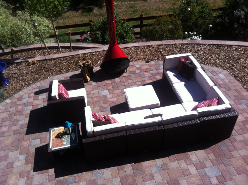 Image of a red dappled stone patio with designed with outdoor furniture and a stand alone wood fire pit.  